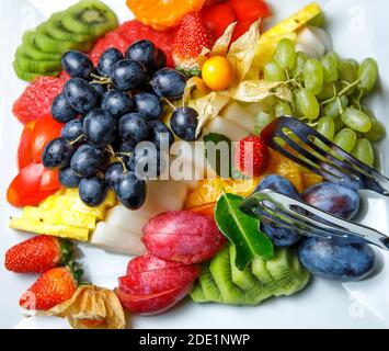 Frutta a fette assortite, uva bianca e nera, kiwi, prugne, ananas, fragole e fisalis sono su un piatto. La vista dall'alto. Foto Stock