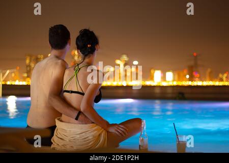 Una coppia al bordo della piscina infinity all'isola di Happiness ad Abu Dhabi, la luce della città lontana di notte Foto Stock