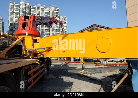 Angolazione inusuale, vista da vicino alla pompa per calcestruzzo carrello con braccio giallo su sito in costruzione in Cina. Edificio residenziale in background. Foto Stock