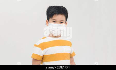 Coraggioso ragazzo teenager con maschera medica in piedi con volto coraggioso isolato su bianco. Infanzia, bambini alla moda, covid-19 lotta Foto Stock