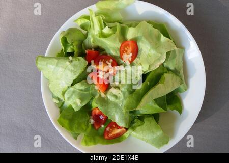 Servita lattuga verde con mini pomodori a fette e aglio fresco, in piatto bianco, dall'alto Foto Stock