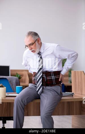 Anziano dipendente che soffre di radicolite sul posto di lavoro Foto Stock