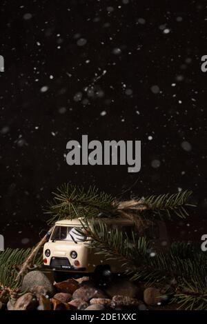 Concetto di Natale. Una piccola macchina giocattolo porta un ramo di un albero di Natale Foto Stock