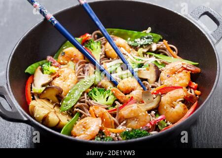 Mescolare gli spaghetti fritti con i gamberi e le verdure in un wok su sfondo scuro Foto Stock