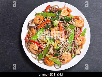 Piatto di noodle fritte Stir con gamberi e verdure su sfondo scuro, vista dall'alto Foto Stock