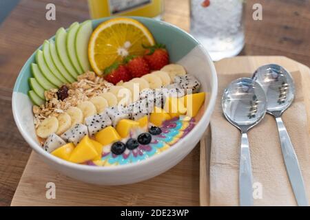 Una sana colazione a base di frullato con muesli, banana tagliata, mele a fette, fragole e vari tipi di noci Foto Stock