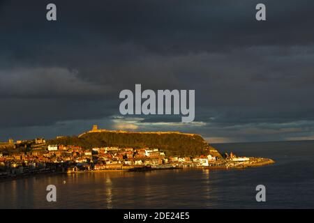 L'ultima luce della giornata a fine novembre, il sole tramontante mette in risalto il promontorio del Castello e il porto e la Città Vecchia di Scarborough, una popolare località turistica Foto Stock