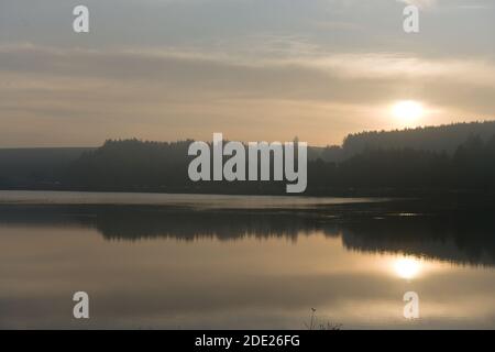 Oltre alle acque calme della sera dei serbatoi di Redmires, una lunga fila di auto sono parcheggiate di fronte a una grande foresta, sotto il caldo tramonto bagliore. Foto Stock