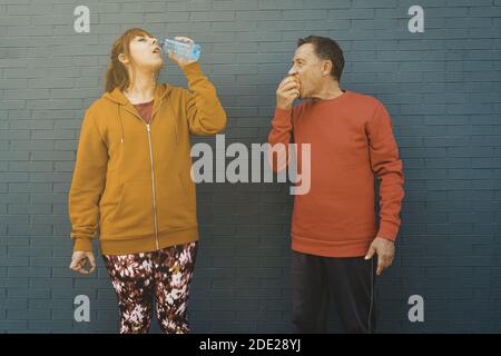 Una femmina di zenzero e un maschio adulto in abbigliamento sportivo bevendo una bottiglia d'acqua e mangiare una mela dolce Foto Stock