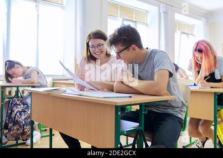 Lezione in classe di studenti delle scuole superiori, insegnante di sesso femminile seduto alla scrivania con lo studente Foto Stock