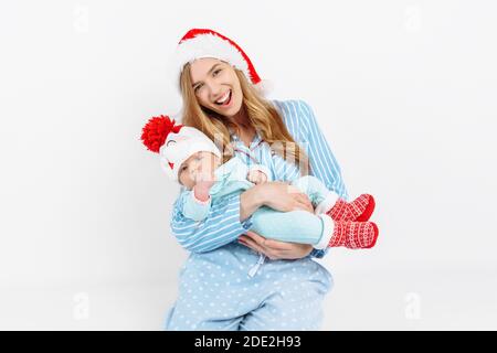 Una giovane madre, il giorno di Natale dà un regalo ad un bambino neonato, una ragazza tiene un bambino nelle sue braccia in un cappello di Natale, mattina di Natale nella famiglia, Foto Stock