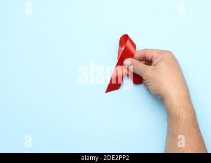 La mano dell'uomo tiene un nastro rosso-simbolo della lotta contro l'AIDS e la vasculite di malattia, primo piano Foto Stock