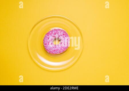 Ciambella rosa con spruzzi rosa sulla piastra. Impasto rosa su sfondo giallo. Vista dall'alto piatto Foto Stock