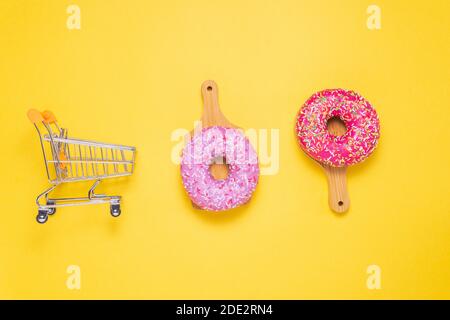 Due ciambelle con glassa di zucchero rosa e cosparse di coloratissime briciole di pasticceria, su sfondo giallo. Il concetto di shopping Foto Stock