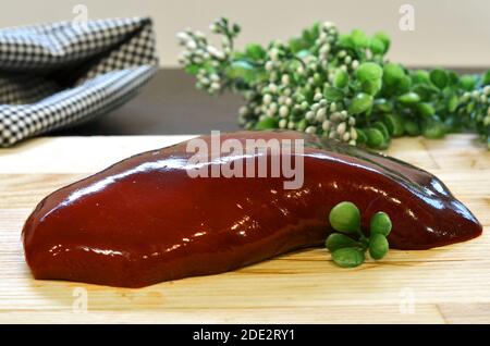 pezzo di fegato crudo un manzo o maiale dall'interno su una tavola di legno, carne d'organo per ricette di pate e molto altro Foto Stock