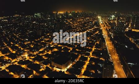 Strade notturne illuminate all'aereo della metropoli di Manila. Edifici moderni, grattacieli e autostrade al crepuscolo del centro cittadino. Filippine città architettura al neon luci in drone shot Foto Stock