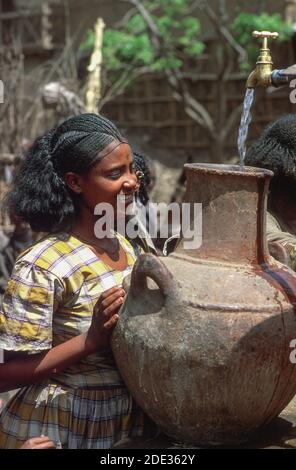 Giovane donna che raccoglie acqua in una grande urna ai rubinetti d'acqua della comunità. Addis Abeba, Etiopia Foto Stock