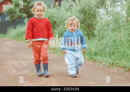 sorella e fratello camminano per la strada in un piccolo villaggio tra le case Foto Stock