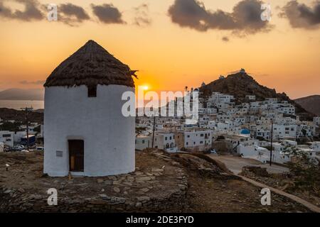 Iconici mulini a vento tradizionali sulla piazza principale di Chora. Tramonto giallo. Collina con piccole cappelle sullo sfondo. Chora, Isola di iOS, Grecia. Foto Stock