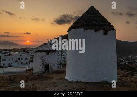 Iconici mulini a vento tradizionali sulla piazza principale di Chora. Tramonto giallo. Collina con piccole cappelle sullo sfondo. Chora, Isola di iOS, Grecia. Foto Stock