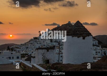 Iconici mulini a vento tradizionali sulla piazza principale di Chora. Tramonto giallo. Collina con piccole cappelle sullo sfondo. Chora, Isola di iOS, Grecia. Foto Stock