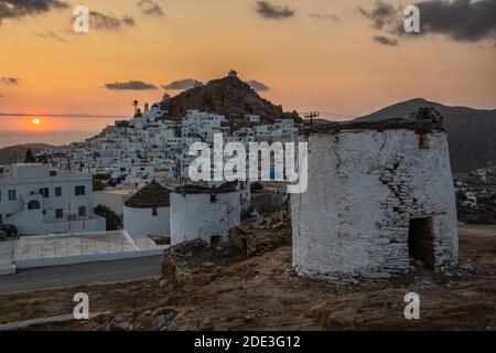 Iconici mulini a vento tradizionali sulla piazza principale di Chora. Tramonto giallo. Collina con piccole cappelle sullo sfondo. Chora, Isola di iOS, Grecia. Foto Stock