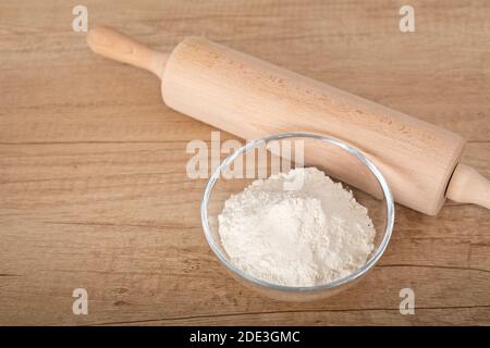 Immagine di farina bianca in recipiente di vetro e coppiglia su sfondo di legno Foto Stock