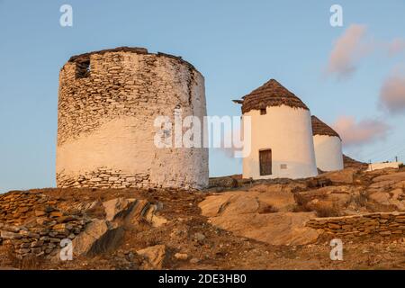 Iconici mulini a vento tradizionali sulla piazza principale di Chora. Tramonto giallo. Collina con piccole cappelle sullo sfondo. Chora, Isola di iOS, Grecia. Foto Stock