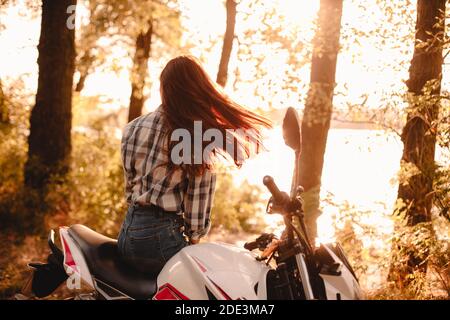 Giovane donna che lancia i capelli mentre si rilassa seduto sul motociclo vicino fiume Foto Stock
