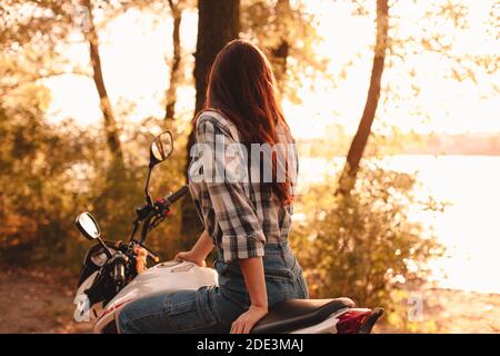 Giovane donna che guarda la vista mentre si siede su moto rilassante dal fiume Foto Stock