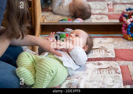 Una madre che interagisce e gioca con la sua bambina di 4 mesi, con entrambe sdraiate su un tappeto da gioco con uno specchio dietro, Regno Unito Foto Stock