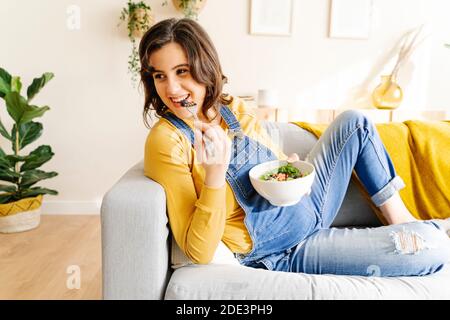 Giovane donna incinta e mangiando un'insalata su un divano. Concetto di maternità Foto Stock