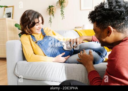 Marito stracciò il ventre della moglie incinta su un divano. Concetto di coppia interrazziale Foto Stock