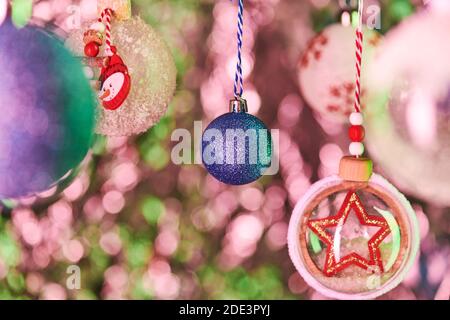 Decorazioni sferiche blu ricoperte di minuscoli luccichini, palline decorative con neve artificiale e stella appesa davanti alla telecamera su sfondo colorato Foto Stock