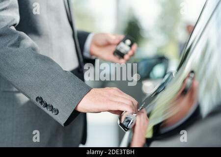 Mano di giovane elegante venditore di nuove auto con telecomando sistema di allarme di controllo in piedi da una delle automobili e andare per aprire lo sportello Foto Stock