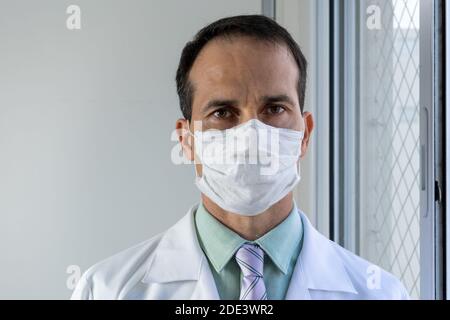 medico di 44 anni con maschera, cappotto bianco e cravatta. Foto Stock