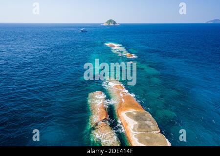 Vista aerea di una barca da immersione vicino a una stretta barriera corallina tropicale e piccola isola nel Mare delle Andamane. Foto Stock