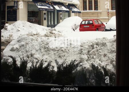 Centro di Bucarest, Romania. Auto parcheggiate di fronte a un'azienda, coperte di neve. Mucchi di neve al bordo della strada. Foto Stock