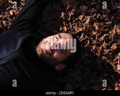 giovane uomo sdraiato su un pavimento di foresta in autunno Foto Stock