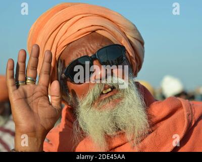 La vecchia baba indù hindù con turbano arancione e occhiali da sole scuri solleva la sua mano destra per salutare e offrire una benedizione. Foto Stock