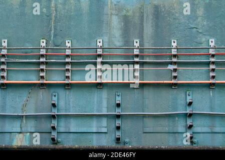 Cavi elettrici multicolore che corrono orizzontalmente lungo una parete blu grigia lungo una linea ferroviaria della metropolitana di Londra. Foto Stock