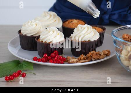 Vista in primo piano del panettiere che decorano gustosi cupcake con parte superiore cremosa Foto Stock