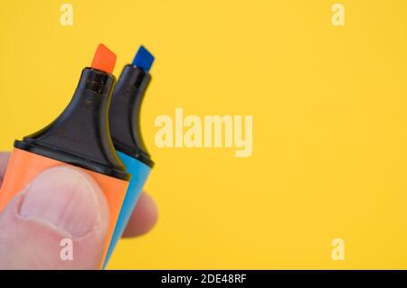 Un colpo di un dito maschio che tiene due marcatori colorati isolato su uno sfondo luminoso Foto Stock