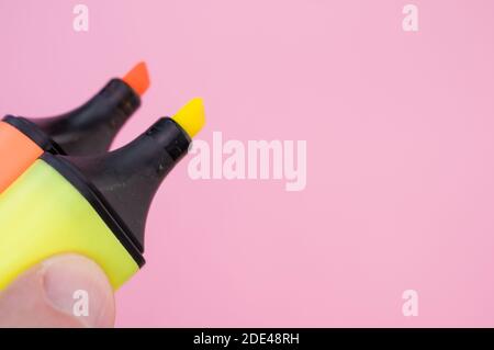 Un colpo di un dito maschio che tiene due marcatori colorati isolato su uno sfondo luminoso Foto Stock