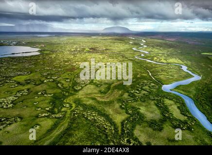 Ampia pianura verde con fiume, meandro, dietro le montagne con drammatiche nuvole e pioggia al lago Myvatn, Skutustaoir, Norourland eystra, Islanda Foto Stock