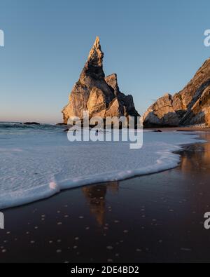 Rocce marcate sulla spiaggia di Praia da Ursa con riflessi e acqua di mare schiumosa, Ulgueira, Portogallo Foto Stock