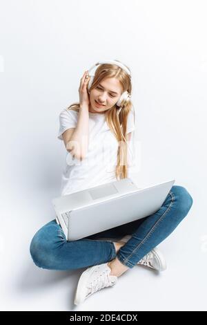 Ragazza allegra che lavora al computer e ascolta la musica, isolata su sfondo bianco Foto Stock