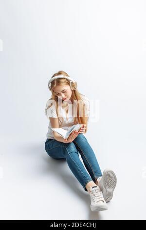 Allegra ragazza che ascolta musica e legge un libro preferito, closeup isolato su sfondo bianco, Foto Stock