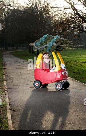 Carina bambina di cinque anni, Firenze, raffigurata come un Elf di Natale e consegnando un piccolo albero di Natale sulla sua classica auto rossa Little Tikes, Regno Unito. Foto Stock