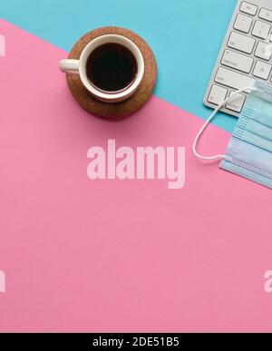Tazza di caffè accanto alla maschera facciale e alla tastiera sul piano portapaziente rosa e blu. Spazio di copia. Foto Stock